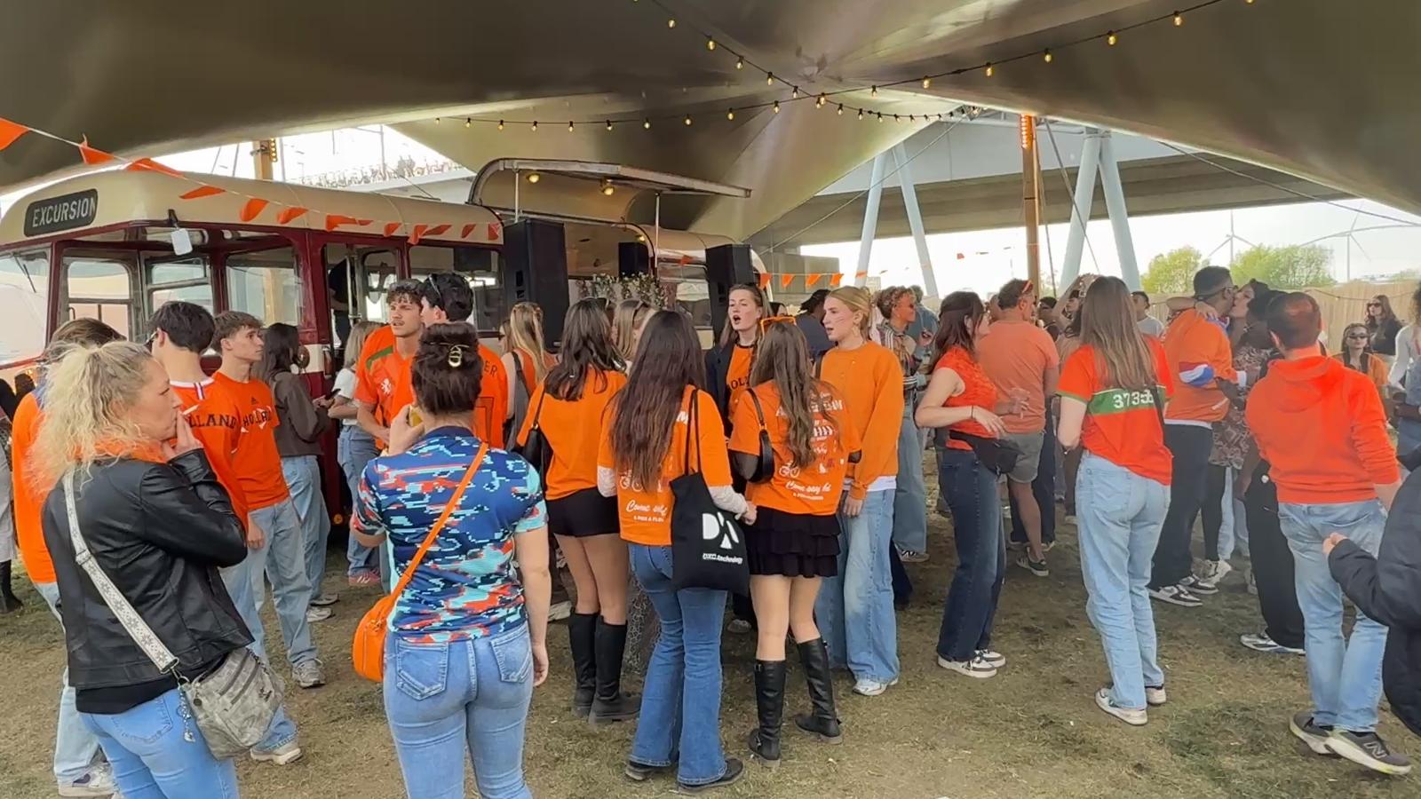 Publiek in oranje danst voor de bus